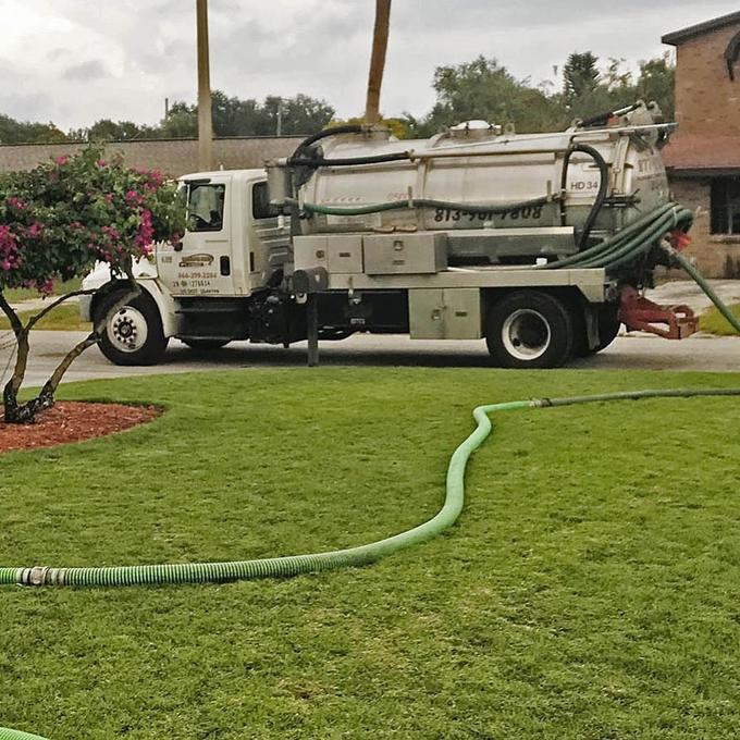 Septic pump truck at the curb with hoses run across a Tampa front lawn